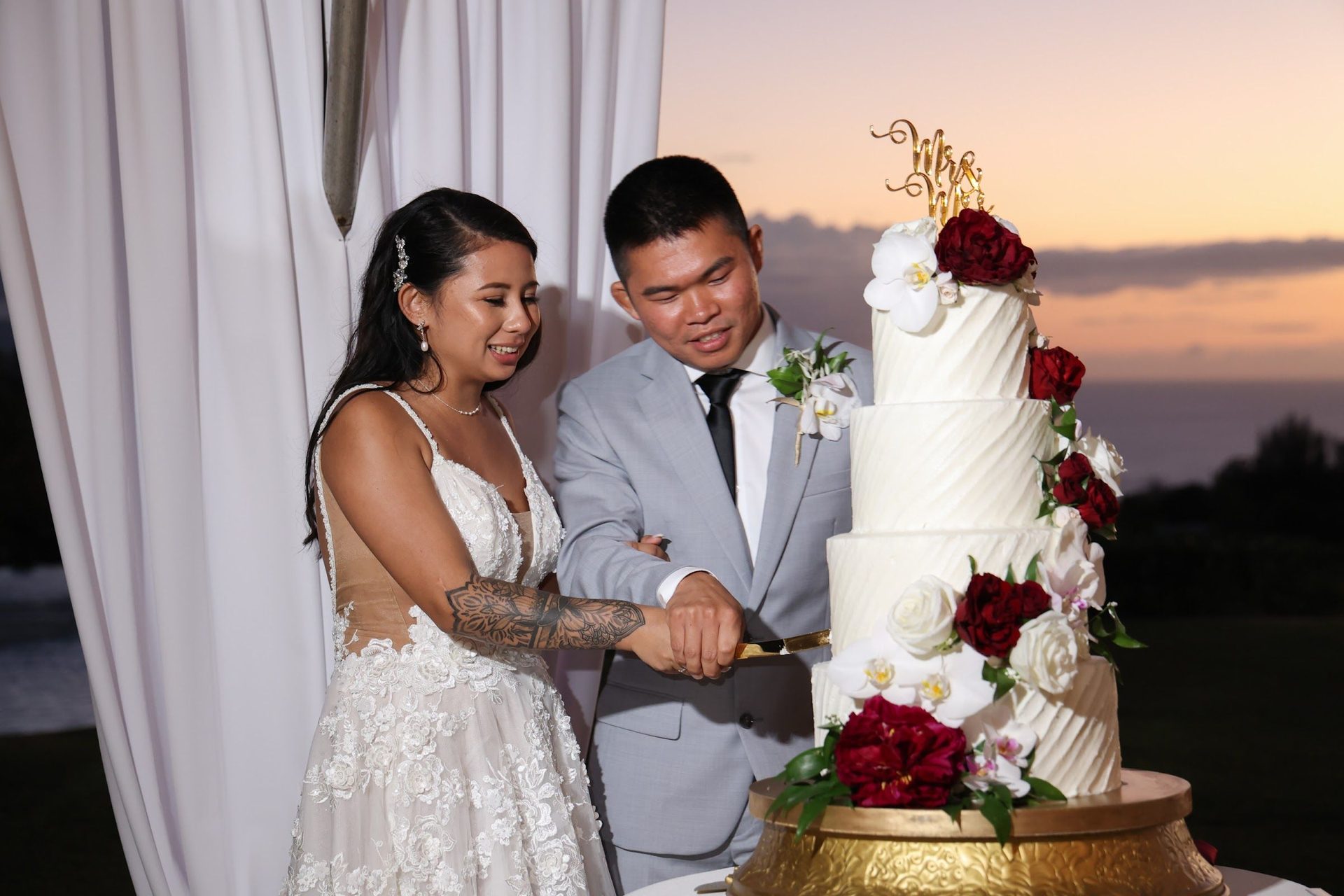 Couple cutting the cake beside floor-to-ceiling windows at sunset