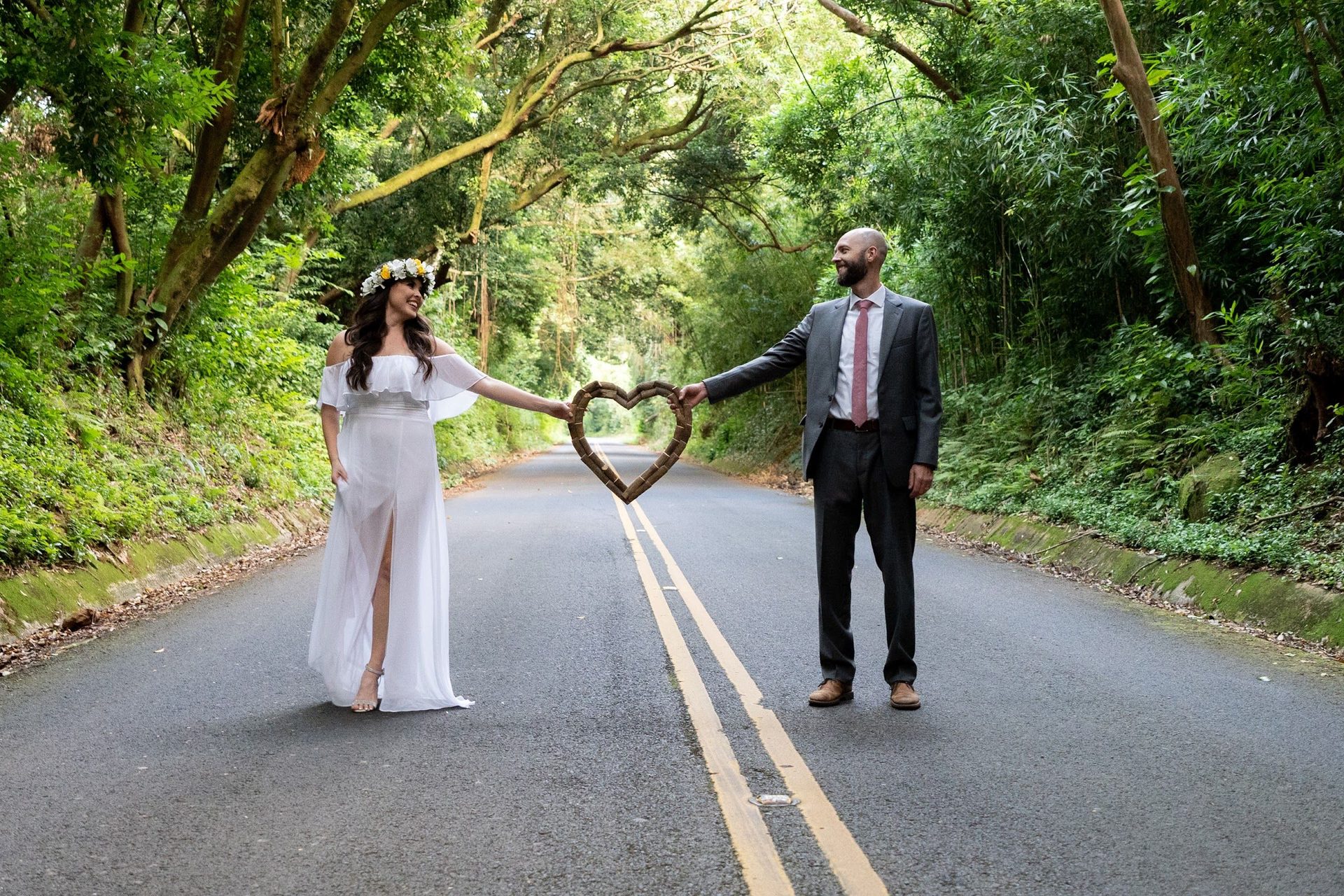Couple forming a heart with their hands on a road surrounded by jungle